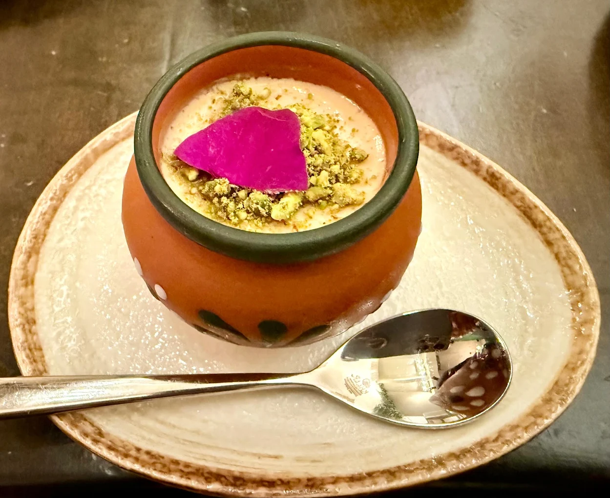 Mishti dahi in a clay pot topped with pistachios and a rose petal