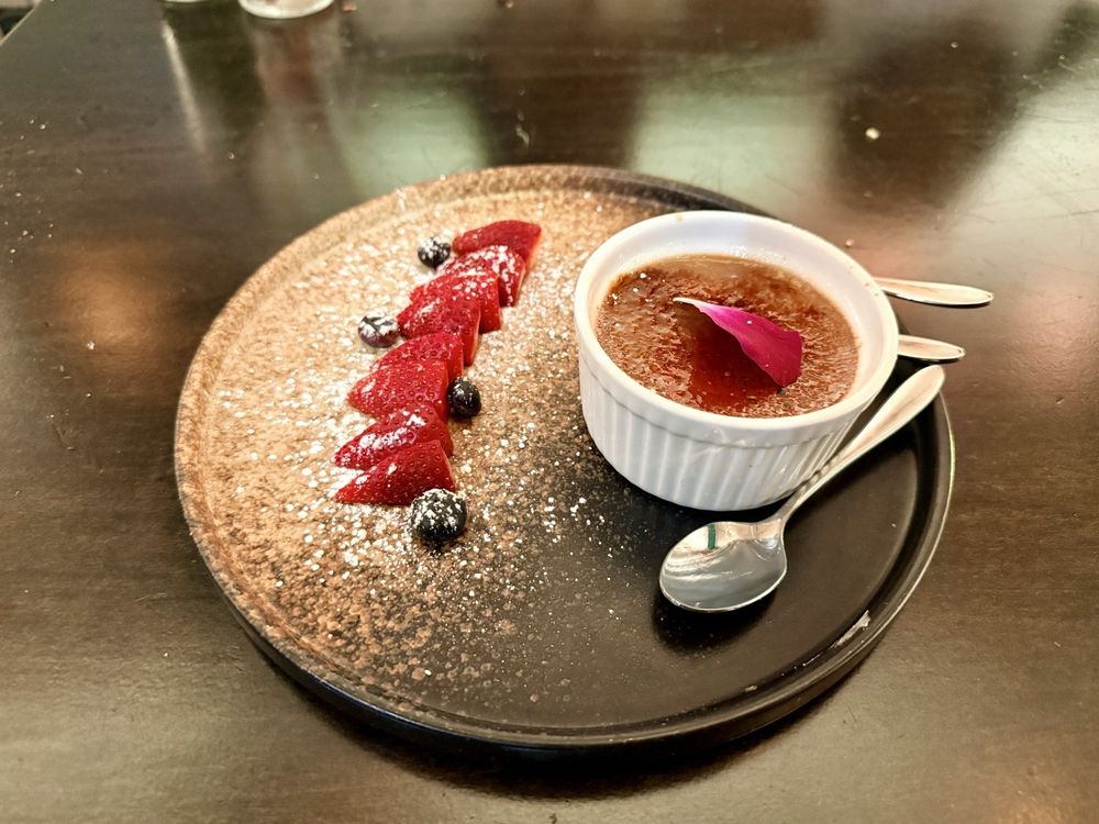 Assam tea crème brûlée in a white bowl with a caramelized top, fresh raspberries and blueberries, pistachios, and a gold leaf
