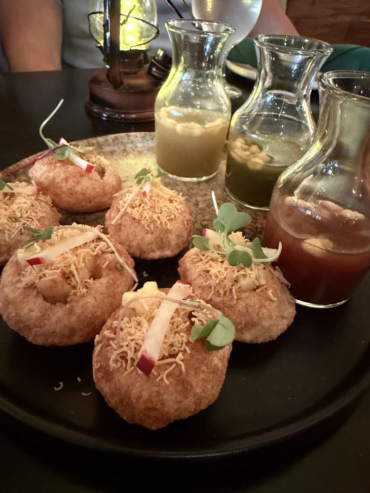 Mango Mirage — crispy pani puris topped with sev and micro greens, beside carafes of spiced mint and tamarind water